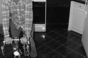 a man in a flannel shirt is riding a bike in a kitchen and smiling