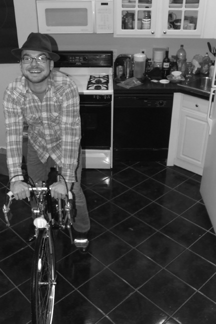 a man in a flannel shirt is riding a bike in a kitchen and smiling