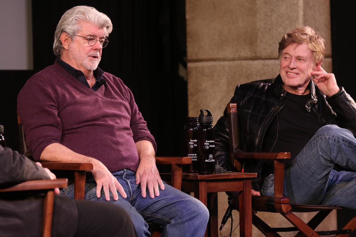 Two men (George Lucas left, Robert Redford right) sit in directors chairs