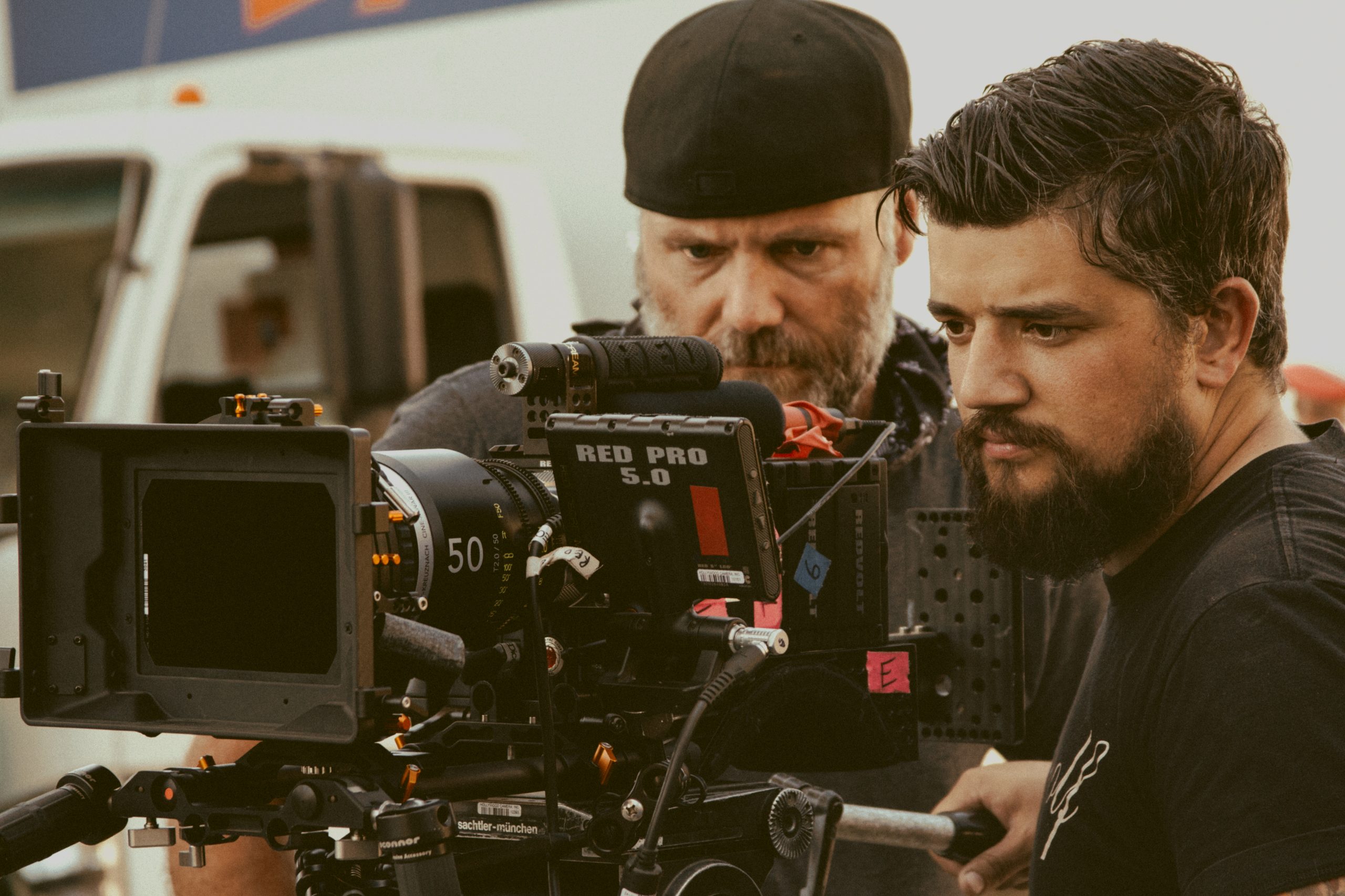 Two men stand behind a film camera.