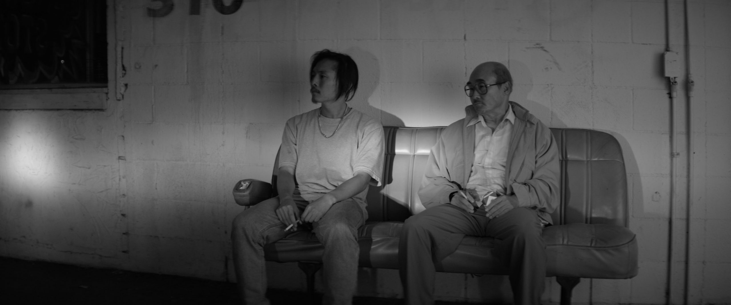 Still image from the movie Gook, with two men sitting on a couch. 