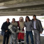 Three men in normal clothes pose with a man dressed as Santa and a man dressed as a koala bear