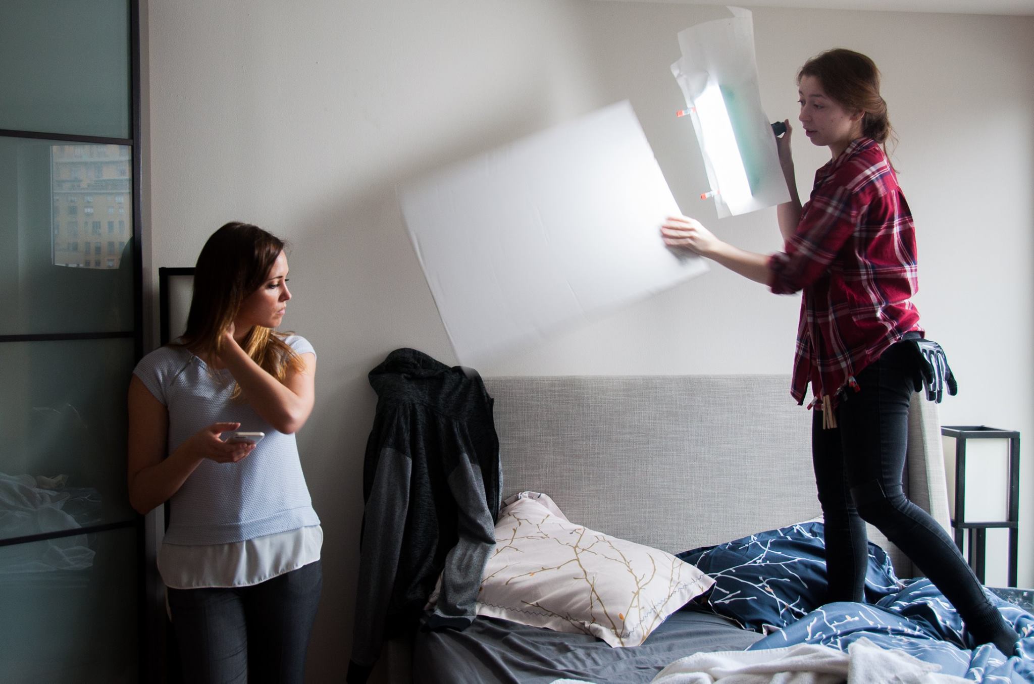 Terra Mackintosh stands in bedroom as character Ali while gaffer, Rebecca Share, lights the scene.