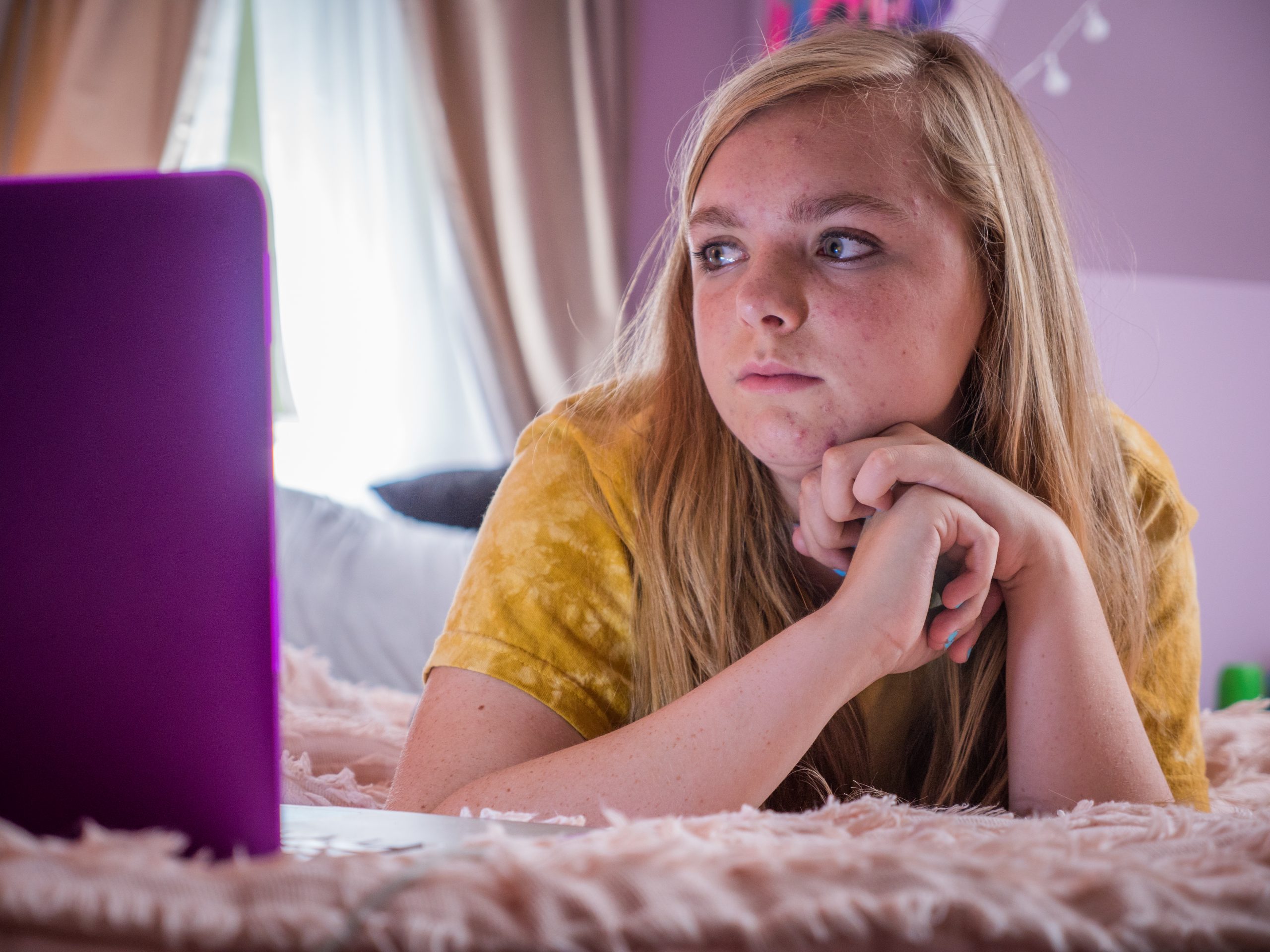 Elsie Fisher as Kaylie in the movie Eigth Grade laying on her bed looking at her computer.