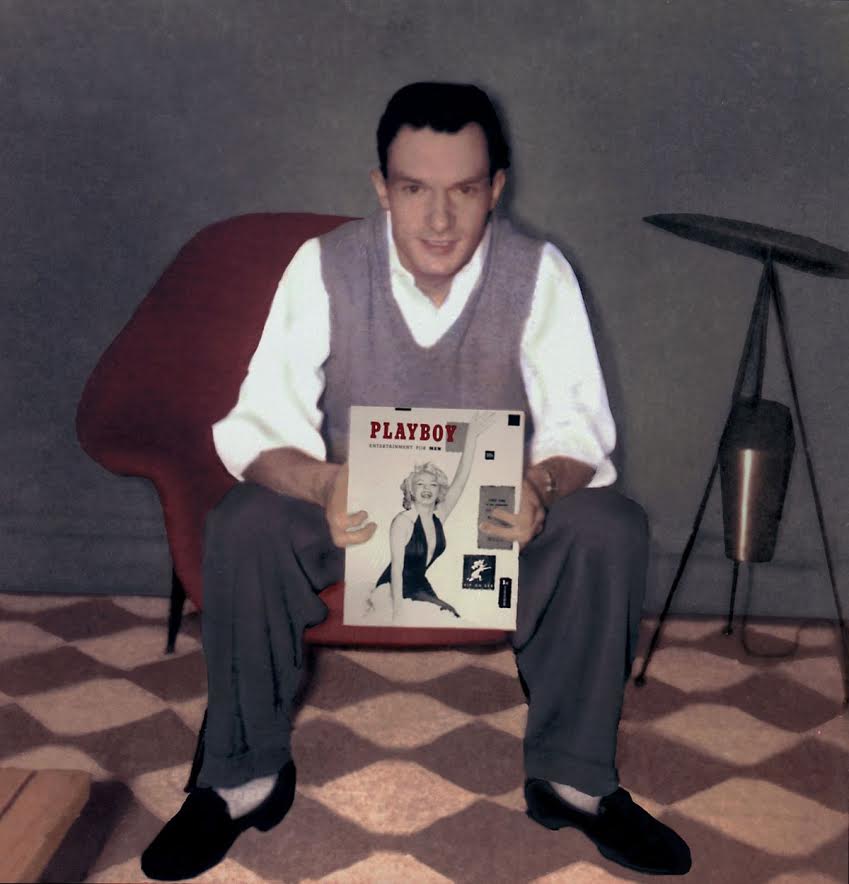 Hugh Hefner sits in a chair, holding the first issue of Playboy Magazine.