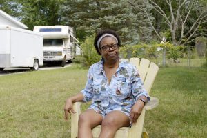 An older African American woman with dark framed glasses sits in a lawn chair in her yard during an interview in the documentary Yours in Sisterhood.