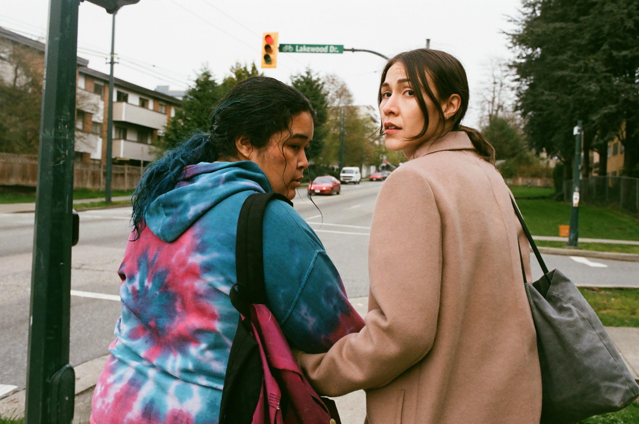 Two women linking arms turn around as they walk down a street.