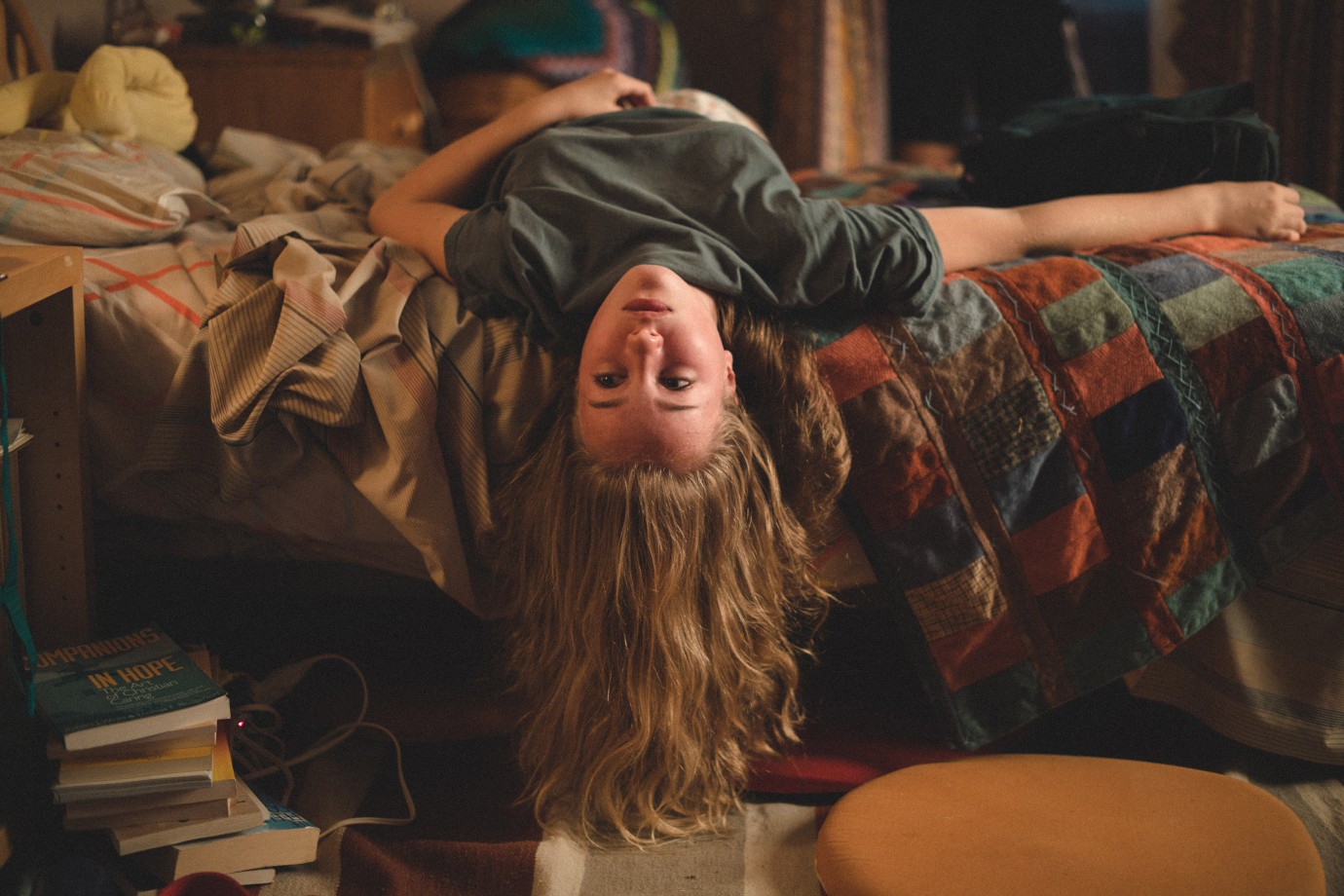 A girl hanging upside down on her bed.
