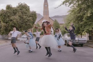 A dance scene from the film Kanarie where Schalk Bezuidenhout is dressed in a wedding dress leading a line of dancers in the street.