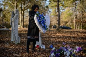 Claudia Lacy at her son Lennon's grave with a heart on a stand made of blue and white flowers