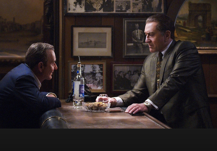 Joe Pesci and Robert De Niro leaning across a table to talk to each other in the movie The Irishman