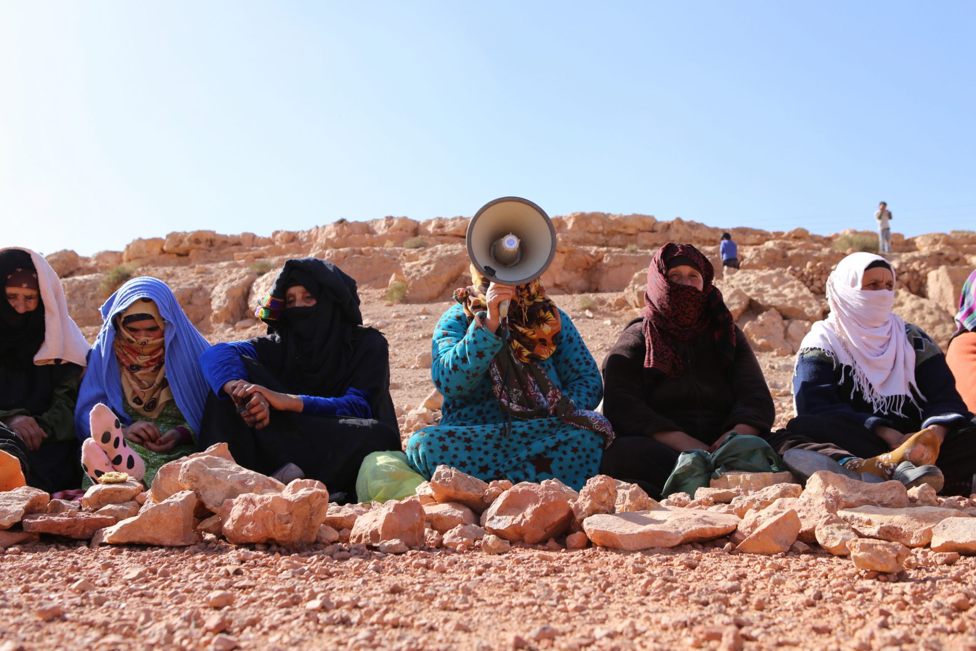 Moroccan women sit in a line while one woman with a megaphone leads a protest