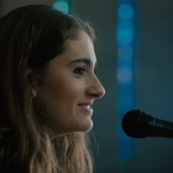 Rachel Sennott faces a microphone in her synagogue in the film Tahara