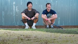 Two men rest outside while holding tennis rackets. 