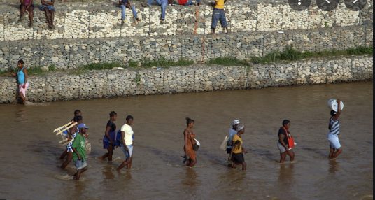 People walking through water near a wall.