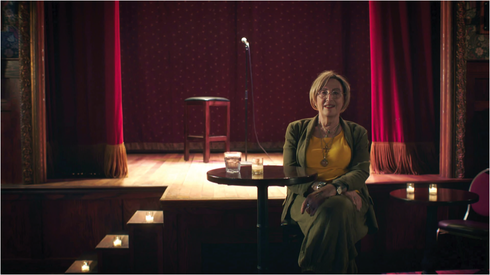 Kate Bornstein in front of lit stage.