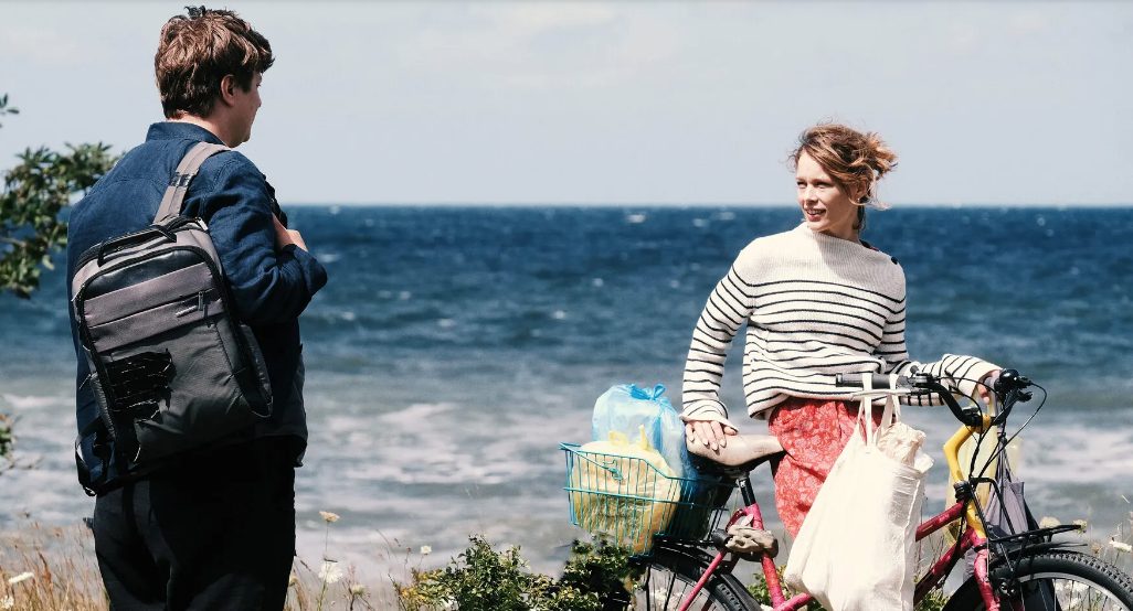 Standing man and woman on bicycle.