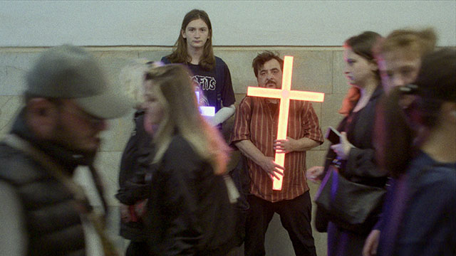 Two men holding a neon crucifix.