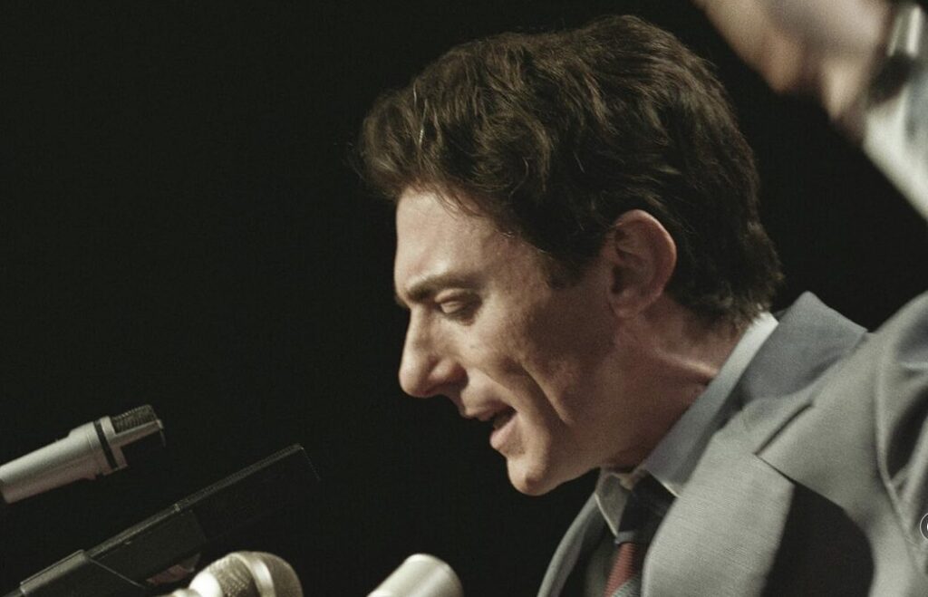 Man speaking to microphones.